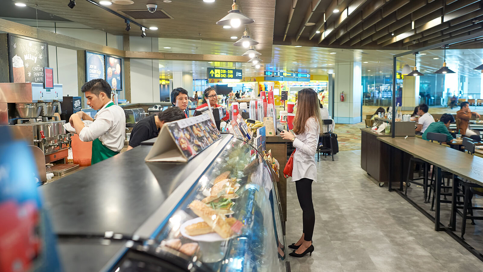 Fresh coffee being prepared at a busy airport cafe, with customers ordering and enjoying food, highlighting the welcoming environment and the importance of kindness and hospitality.