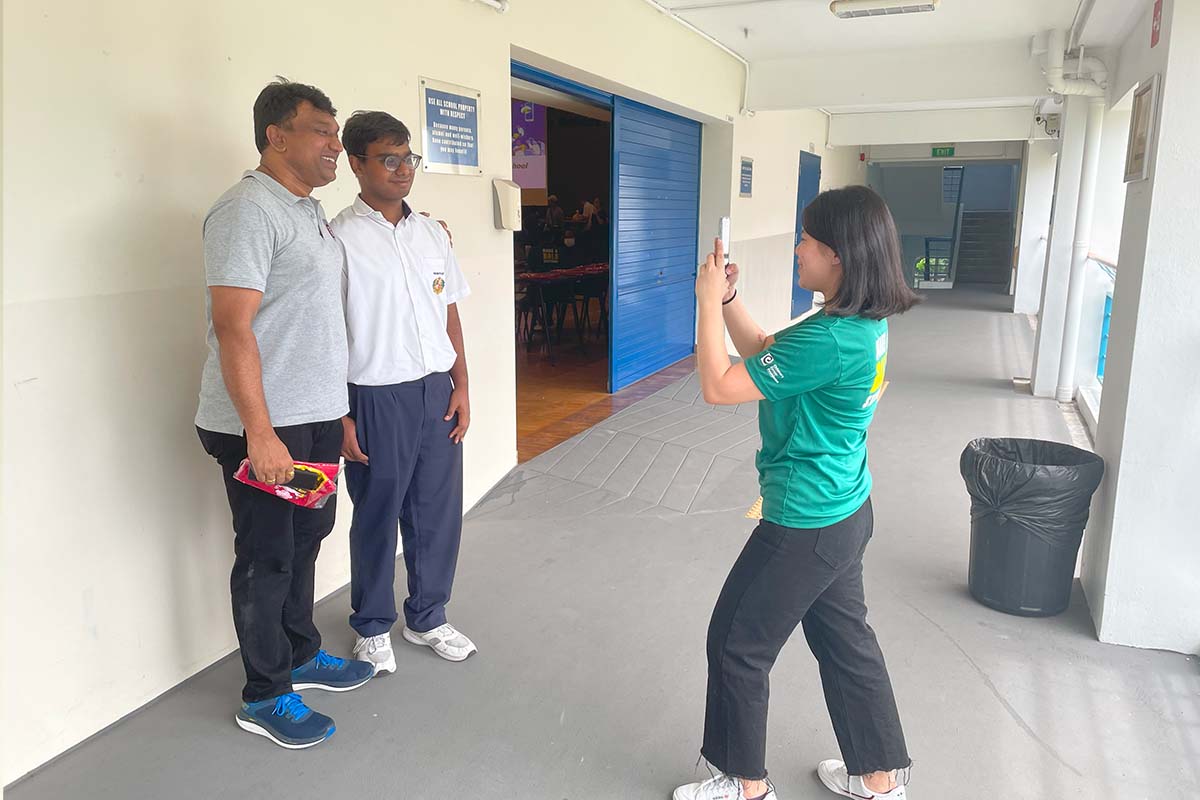 Smiling girl taking a photo of two men in a school corridor, promoting kindness and inclusivity.