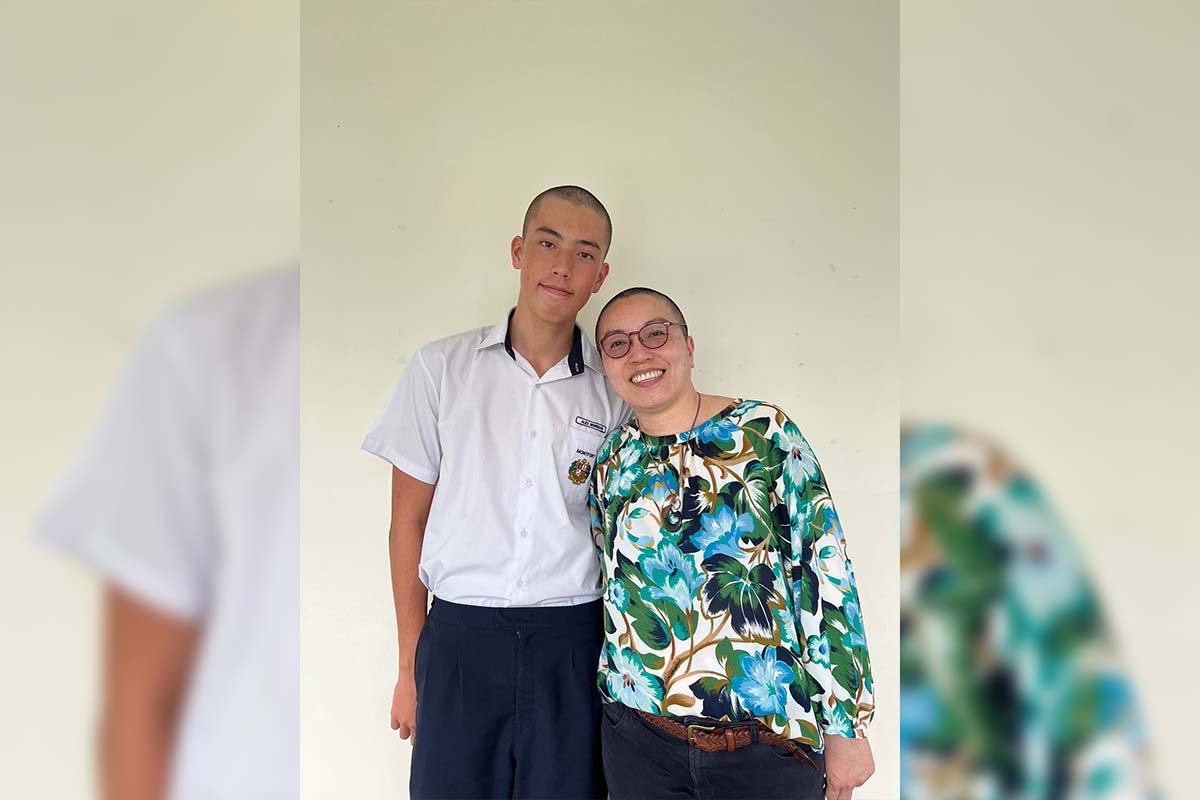 A young male student in a school uniform standing next to a smiling woman with glasses and a colorful floral blouse, representing kindness and inclusivity in Singapore.