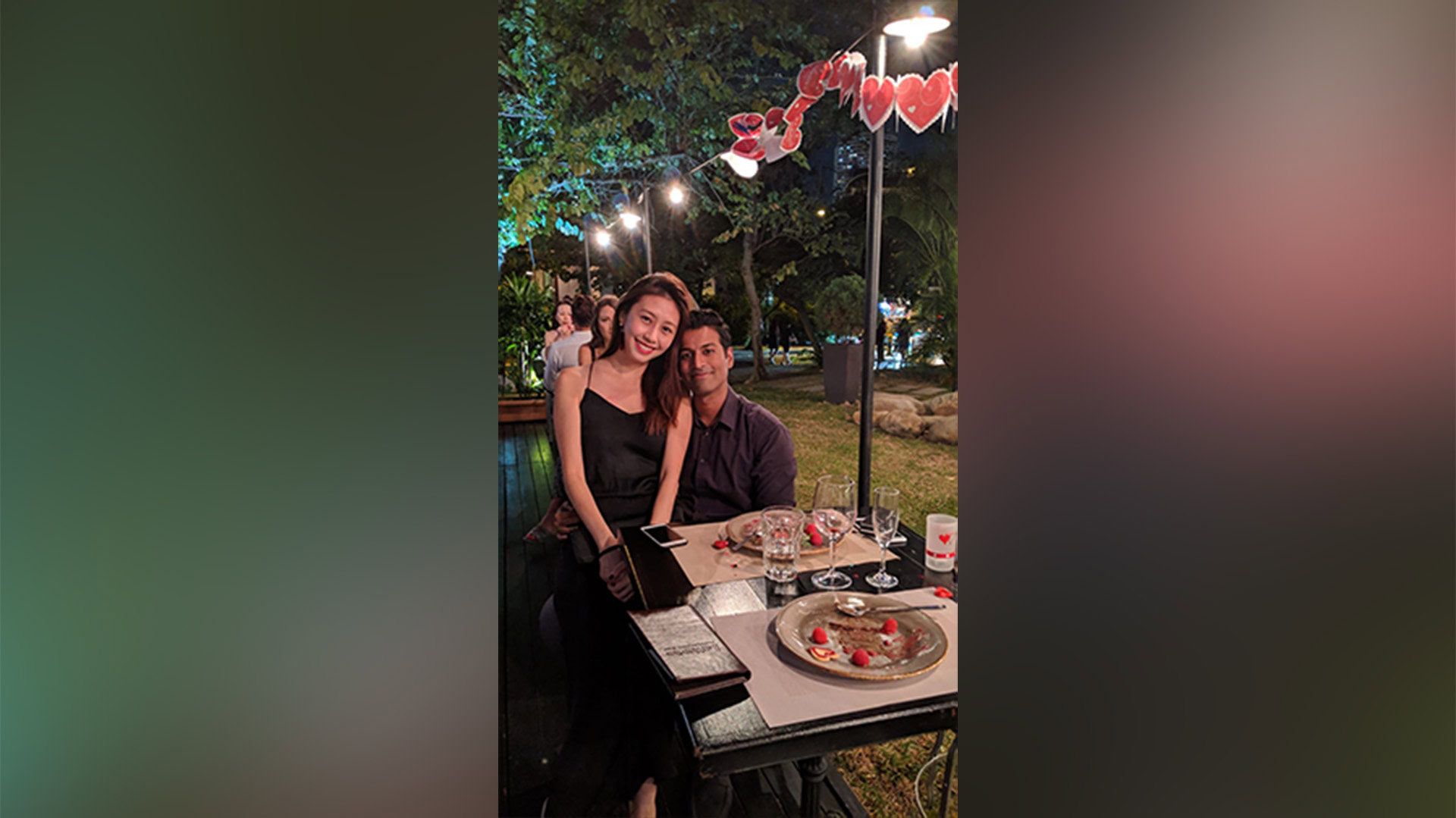 Romantic couple celebrating at an outdoor dinner during Pride, with Love-themed decorations and a festive ambiance, emphasizing kindness and acceptance.