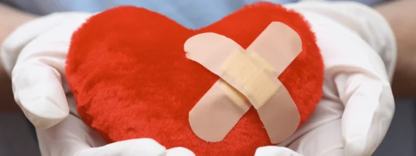 A plush heart with a plaster on it being held by two hands