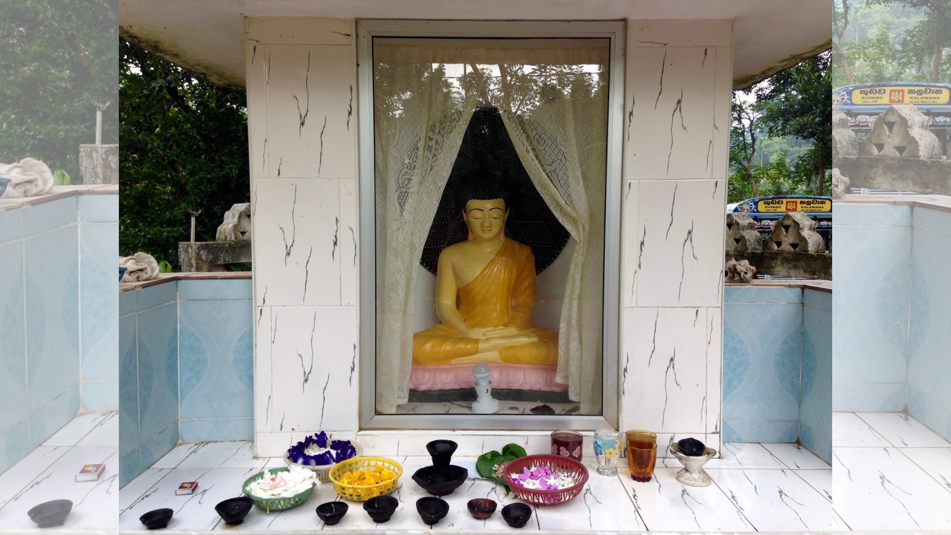 Meditating Buddha statue inside a small shrine, surrounded by offerings and flowers, promoting kindness and mindfulness in Singapore.