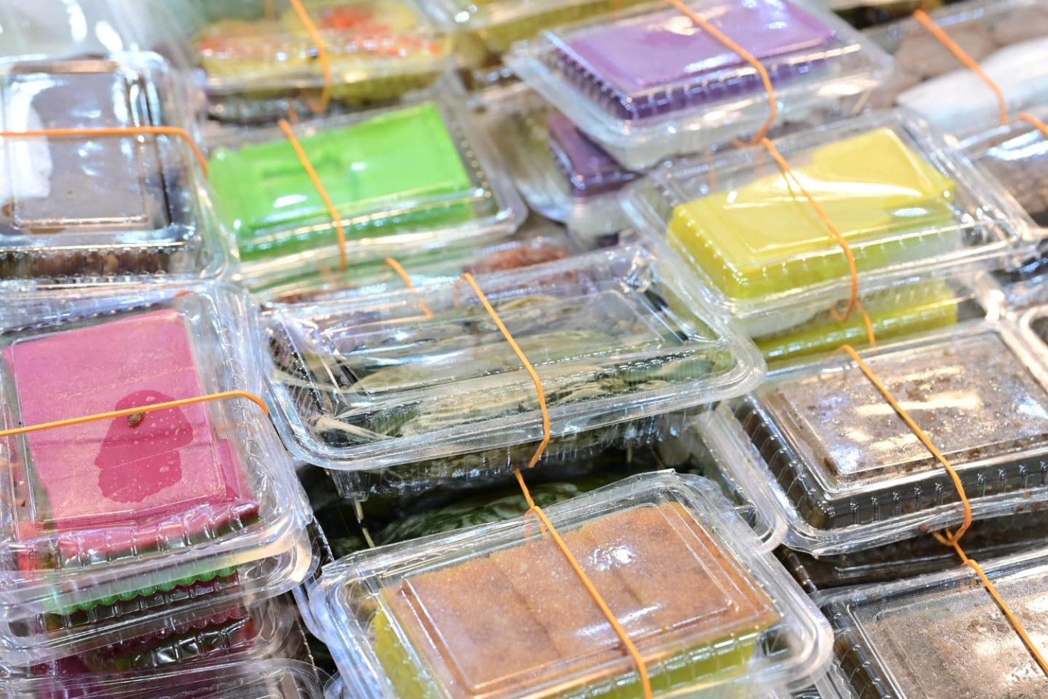 Colorful traditional snacks wrapped in plastic containers, highlighting Singapore's diverse food culture and community spirit.