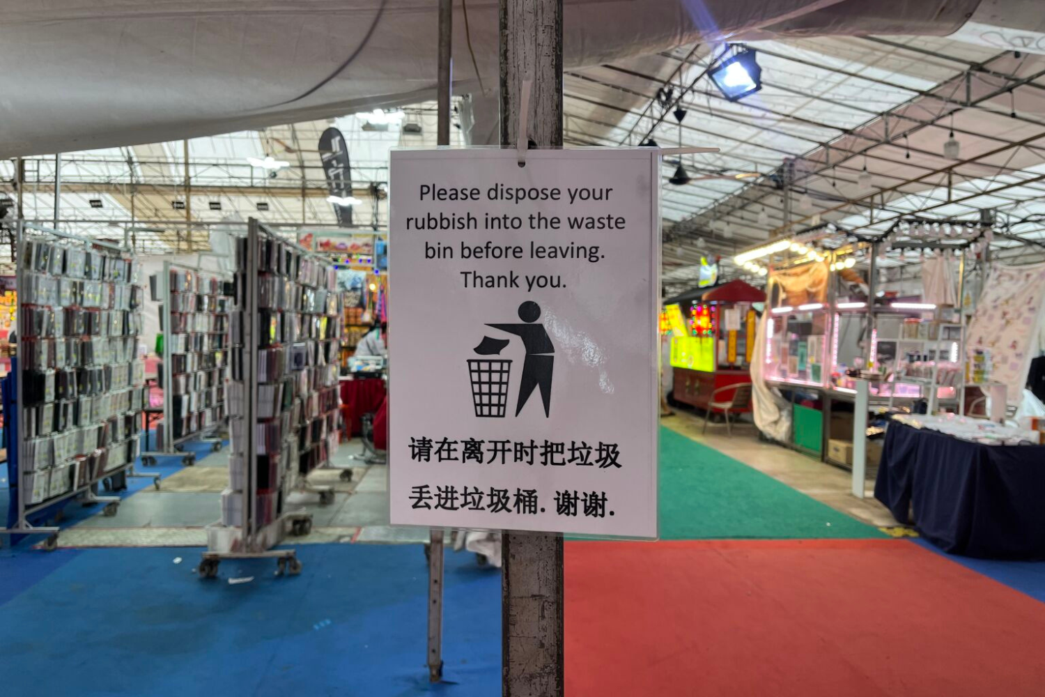 Recycling bin sign at a market or fair, encouraging proper disposal of rubbish before leaving.