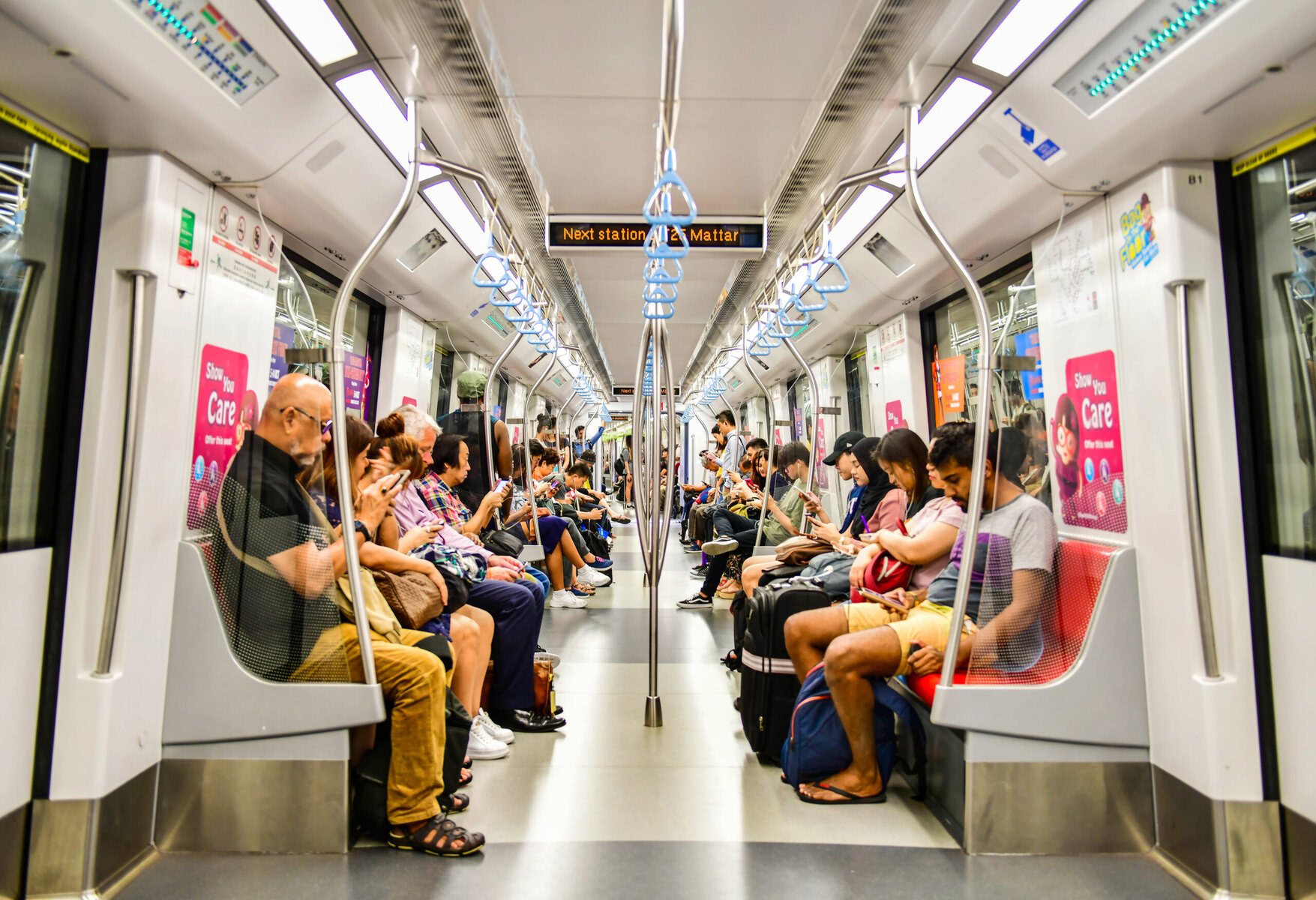 A diverse group of passengers seated inside a metro train, some engaged with their phones, others resting, illustrating inclusivity and community in Singapore's public transportation.