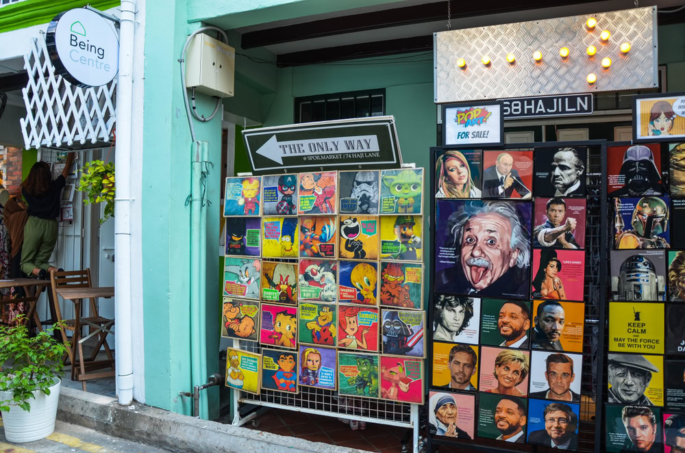 An outdoor art display featuring colorful Pride-themed artwork and portraits in Haji Lane, Singapore, promoting kindness and inclusivity.