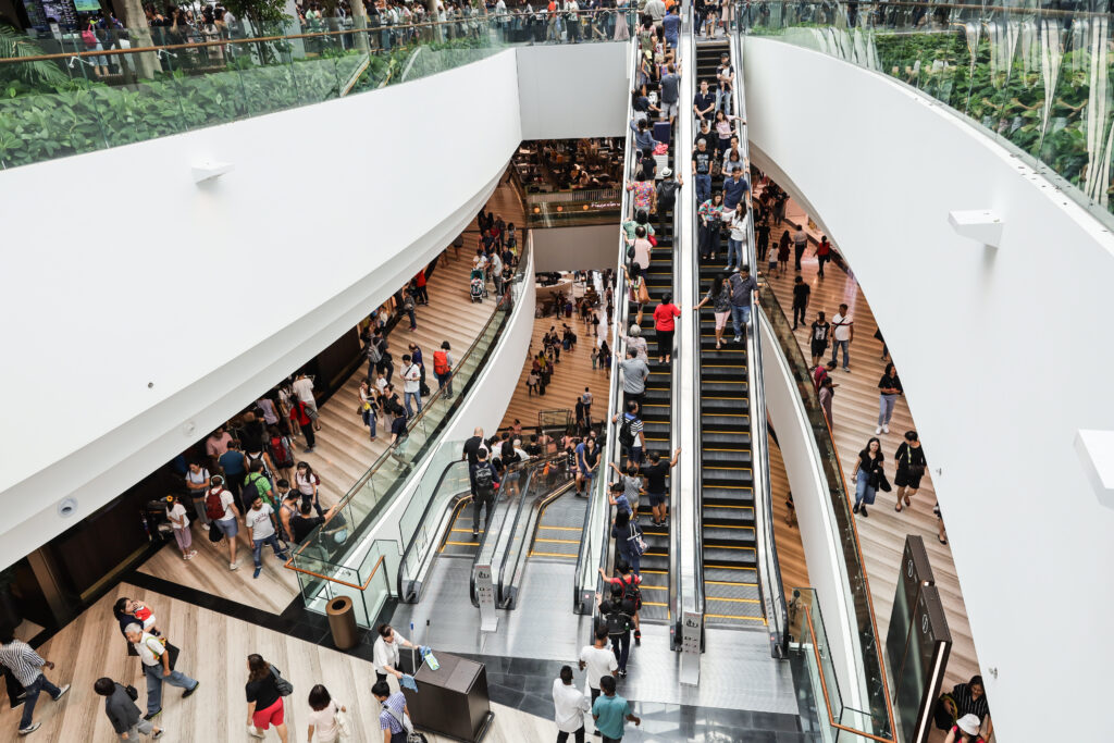 A busy shopping mall with escalators filled with shoppers on multiple levels, showcasing modern architecture and vibrant activity.