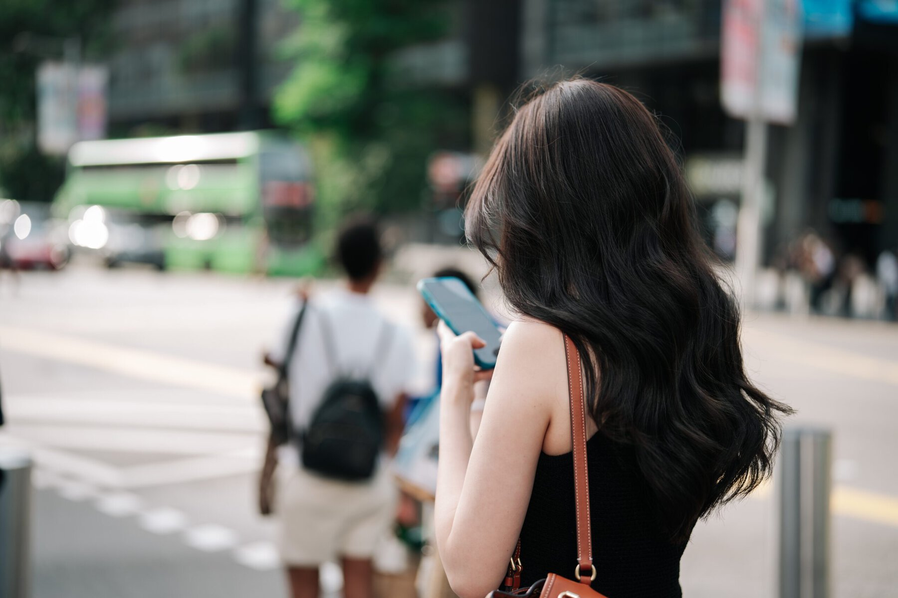 Young woman with long dark hair looking at her smartphone on a busy city street in Singapore.
