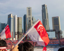 Crowd waving Singapore flags during National Day celebration in front of Singapore's skyline.