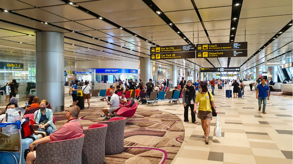 Busy scene at Singapore Changi Airport with travelers, seating areas, and signage for bus, coach, and departure gates.
