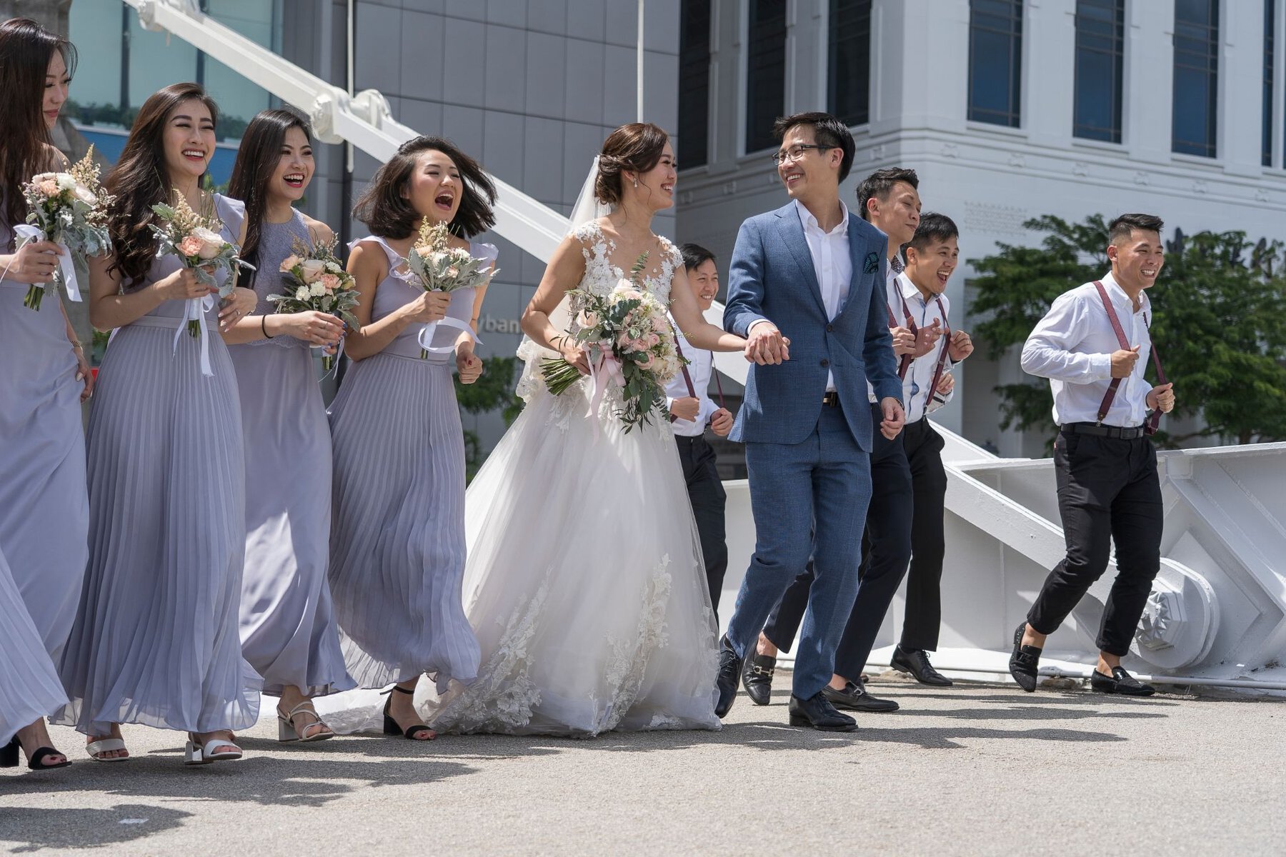 Happy wedding celebration with bride, groom, bridesmaids, and groomsmen outdoors in Singapore, showcasing diversity and joy.