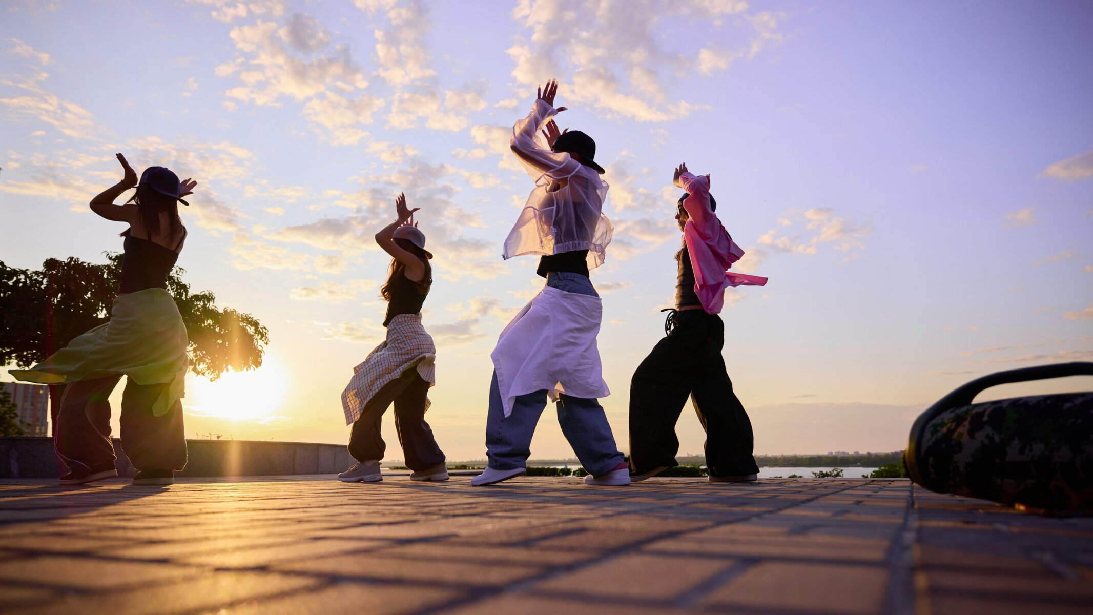 Group of K-pop dancers performing at sunset near Singapore landmark, showcasing vibrant outfits and energetic dance moves.