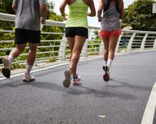 Three people running together on a paved road with greenery in the background, promoting health and community connection.