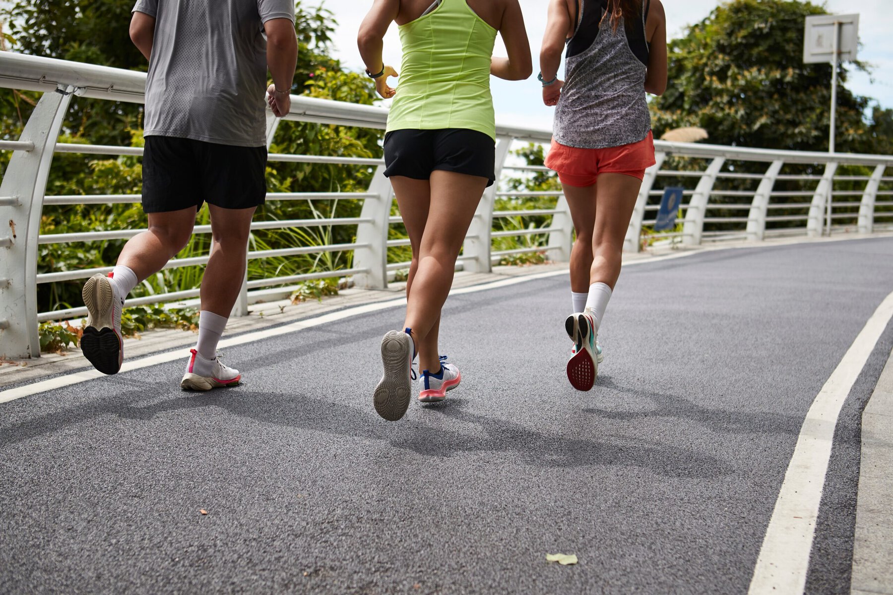 Three people running together on a paved road with greenery in the background, promoting health and community connection.