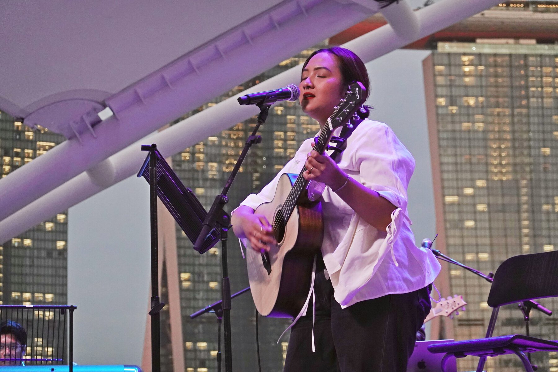 A young woman performs with guitar and microphone at Singapore Pride event, celebrating kindness and diversity.